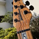 Detail hlavy dřevěné elektrické kytary v přirozené barvě. Na dřevě je vidět nápis MUSICMAN a vedle něj svisle orientovaný text STEREO BALL. V horní č…