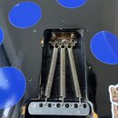 Fotografie zachycuje zadní část elektrokitary s černým povrchem a modrými kruhy. Je vidět mechanismus kobylky se třemi kovovými pružinami a kovovou z…