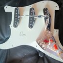 Bílý pickguard s třemi černými snímači typu single-coil a viditelným zapojováním s potenciometry a kondenzátory. Na snímačích jsou ručně napsané popi…