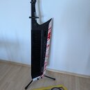 Černý keytar s bílým bočním panelem, který je zdoben červenými skvrnami připomínajícími krev. Na krku je svisle napsáno AX-Edge a v dolní části těla…