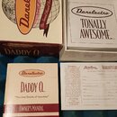 Fotografie zobrazuje originální krabici, vnitřní obal a doprovodné dokumenty od značky Danelectro. Na krabici je nápis „DADDY O“ a slogan „The Grand…