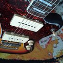 Detail elektrické kytary s barevným přechodem těla od červené přes oranžovou k žluté. Nástroj má tmavě červenou zrcadlovou pickguard s dvěma bílými s…
