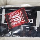 Fotografie zachycuje černý papírový nebo kartonový materiál v průhledném plastovém obalu. Na povrchu je bílý nápis s viditelnými písmeny "B", "E" a "…