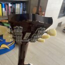 Záběr na zadní stranu tmavě hnědé hlavy kytary s kovými ladičkami a krémovými plastovými knoflíky. Na povrchu je vidět nápis MADE IN USA a pod ním ne…
