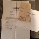 Fotografie zobrazuje několik papírových dokumentů. Na vrchu je oranžová účtenka s nápisy „AMPEG SVT-III PRO“ a „AMPEG SVT-4OHM“. Pod ní je bílý papír…