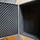 Otevřený hliníkový kufřík s černou vnitřní výplní. Víko je vystlané černou akustickou pěnou s vlnovitým profilem, spodní část je vyložena hladkým čer…
