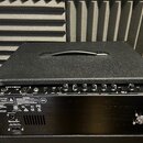 Černý kombozesilovač s texturovaným povrchem a rukojetí na horní straně. Na ovládacím panelu jsou nápisy INPUT, ACTIVE EQUALIZER, OUTPUT a PATCH BAY.…