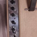 Detailní pohled na ovládací panel kytarového komba s kovovým povrchem. Panel obsahuje nápisy MASTER, CHANNEL SELECT, MIDDLE, BASS, TREBLE, DRIVE, VOL…