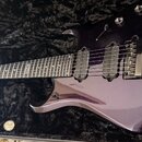 Fialová elektrická kytara v černém polstrovaném kufru. Na hmatníku je viditelný nápis "Custom Shop". Kytara má dva snímače typu humbucker a fixní mos…