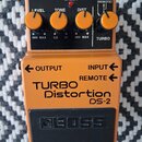 Kytarový efekt pedál oranžové barvy s černým ovládacím panelem a černým stoupákem. Na pedálu je nápis TURBO Distortion DS-2 a logo BOSS. Ovládací pan…