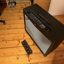 Černý kytarový kombozesilovač s šedou textilní maskou předu. Na horním ovládacím panelu je nápis MUSTANG IV a logo Fender. Vedle zesilovače leží čern…