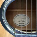 Detail zvukové otvory akustické kytary s dřevěnou deskou. Uvnitř otvoru je vidět bílá štítková nálepka s nápisy YAMAHA a APX-7A. Okraj otvoru je zdob…