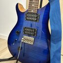 Modrá elektrická kytara s výraznou strukturou dřeva a dvěma humbuckery. Na hmatníku jsou viditelné vložky ve tvaru hvězd. Kytara je umístěna na černé…