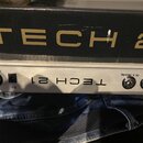 Stříbrné zařízení s nápisem TECH 21. Na předním panelu jsou vlevo konektor OUTPUT a vstup D.C., vpravo konektory IN A (MAIN) a IN B. Nad přístrojem j…