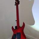 Zadní pohled na červenou elektrickou kytaru s lakovaným povrchem. Na hlavě hmatníku je viditelné logo v kruhu a nápis "STRATOCASTER". Tělo kytary má…