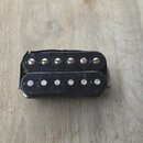 Černý humbucker s dvěma řadami šesti magnetických pólů. Horní řada pólů je kovová, spodní řada je bílá. Na komponentu nejsou vidět žádné značky ani n…