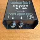 Černá pasivní DI box s nápisem DEXON NS 100 a popisem Professional Single-Channel Passive Direct Box. Na horní straně jsou označení INPUT 50K ohm, PA…