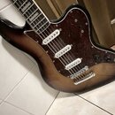 Elektrická kytara s trupem v tmavě hnědém sunburst provedení a tmavě hnědou želvovinou pickguardem. Nástroj má tři bílé snímače typu single-coil a je…