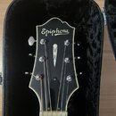 Černá hlava kytary s bílým lemováním, umístěná v černém tvrdém pouzdře. Na horní části je bílý nápis Epiphone a uprostřed bílý symbol ve tvaru kapky.…
