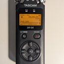 Černý digitální záznamový zařízení s nápisy TASCAM a DR-05. Displej zobrazuje hlášku NO CARD a časovač 00H00M00S. V dolní části je nápis LINEAR PCM R…