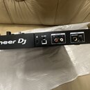 Zadní strana černého DJ mixeru s bílým nápisem Pioneer DJ. Jsou zde viditelné konektory USB, MASTER (R a L) a MIC s popisky UNBALANCED a LEVEL. Zaříz…