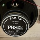 Fotografie zachycuje zadní stranu reproduktoru v dřevěném boxu. Na černém krytu magnetu je bílý nápis E-50-16, 50 Watts a 16 OHM. Pod nimi je logo PR…