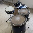 Sada tmavě modrých bubnů s kovovými obručemi. Na blanách několika bubnů je viditelný nápis EVANS. V pozadí je umístěn činel na stojanu. Povrchy blan…