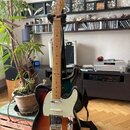 Elektrická kytara s tmelelovým povrchem v přechodu od černé k hnědé a žluté barvě. Na hlavě je viditelné logo Fender. Kytara má bílý pickguard, jeden…