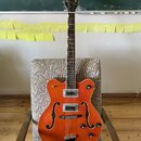 Oranžová polodupatá elektrická kytara s hnědým hmatníkem a bílým lemováním. Na hlavě je bílý nápis GRETSCH a na spodní části korpusu je kovový most s…