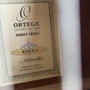 Fotografie zachycuje štítek uvnitř akustického nástroje. Na štítku je logo a nápisy ORTEGA GUITARS EST 1994, FAMILY SERIES a model R121-3/4. Je zde r…