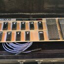 Stříbrný MIDI pedál s černými spínači a dvěma expresními pedály, umístěný v černém kufru. Na horní části je nápis FCB1010 MIDI FOOT CONTROLLER a digi…