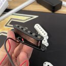 Fotografie zachycuje elektrický snímač typu humbucker s černým plastovým rámečkem a viditelným měděným vinutím. Snímač má šest kovových pólů a jsou z…