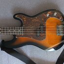 Elektrická basová kytara s korpusem v barevném přechodu od žluté přes oranžovou k černé. Nástroj má hnědý hmatník a tmavě hnědý pickguard s texturou…