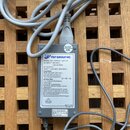 Šedý síťový adaptér s připojeným kabelem, položený na dřevěné mřížce. Na bílém štítku je uveden výrobce FSP GROUP INC., MODEL NO.: FSP048-1AD101M, AC…