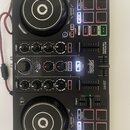 Černý DJ kontrolér s dvěma jog-koly a centrální sekcí s knoflíky a posuvníky. Na přístroji jsou viditelné nápisy Hercules, DJCONTROL IMPULSE 200 a DJ…
