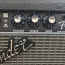 Kytarový kombozesilovač s černým povrchem a stříbrnou textilní maskou reproduktoru. Na ovládacím panelu jsou nápisy INPUT, GAIN, VOLUME, TREBLE, BASS…