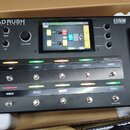 Černý kytarový procesor s displejem a expresním pedálem, umístěný v přepravní krabici. Na zařízení je nápis HEADRUSH PEDALBOARD a v pravém horním roh…