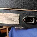 Detail zadní strany černého přístroje s texturovaným povrchem. Na stříbrném štítku je nápis VEB Klingenthaler Harmonikawerke Klingenthal, Deutsche De…