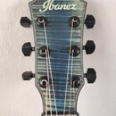 Fotografie zachycuje hlavu elektrické kytary s modrým slupovaným povrchem a bílým lemováním. V horní části je bílý nápis Ibanez. Na hlavě jsou umístě…