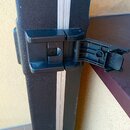 Detailní pohled na černý plastový zámek otevřeného tvrdého kufru. Kufr má černý strukturovaný povrch a stříbrnou kovovou lištu v místě spoje. Na plas…