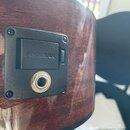 Detailní pohled na černý plastový ovládací panel zapuštěný do tmavého dřevěného povrchu nástroje. Na panelu je vyraženo logo FISHMAN a nachází se zde…