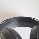 Černé sluchátka s polstrováním z umělé kůže na hlavovém oblouku i na mušlích. Povrch materiálu vykazuje drobné vrásnění a známky používání. Na vidite…