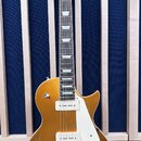 Zlatá elektrická kytara s tmelejším hmatníkem a bílým pickguardem. Na hlavě je bílé logo FGN a nápis Les Custom. Nástroj má dva humbuckery s bílými k…
