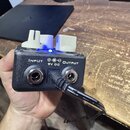Černý efekt pedál s třemi bílými přepínači a modrým svítícím kontrolním světlem. Na přední straně jsou nápisy INPUT, OUTPUT a 9V DC s označením polar…
