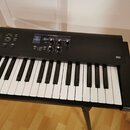 Černý digitální klavír s bílými a černými klávesami. Na ovládacím panelu je nápis PATCH MODIFY, sekce s tlačítky UPPER, LOWER a PROG/BALANCE a čtyři…