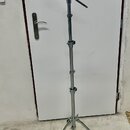 Stříbrný kovový mikrofonní stojan s trojnožkou a teleskopickým stoupacím mechanismem. Horní část obsahuje kloubový ramene s držákem na mikrofon. Na s…