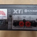 Záhlaví zadní strany černého zesilovače s nápisy Crown, XTi a CLASS 2 OUTPUT. Jsou zde vidět výstupní konektory s červenými a černými krytkami pod ná…