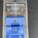 Modrý efekt pedál v originálním plastovém blisteru. Na obalu i na samotném pedálu je uveden název HUSH THE PEDAL a značka ROCKTRON s dopisem TECHNOLO…