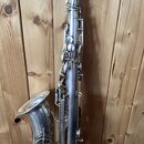 Stříbrný saxofon s kovovým povrchem a dřevěným mouthpiecem. Nástroj vykazuje známky opotřebení v podobě drobných škrábanců a oxidace povrchu. Na těle…