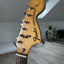 Fotografie zachycuje hlavu elektrické kytary z dřeva s přirozeným povrchem. Na hlavě je černý nápis Fender® STRATOCASTER a drobný text Pat. 3,132,975…